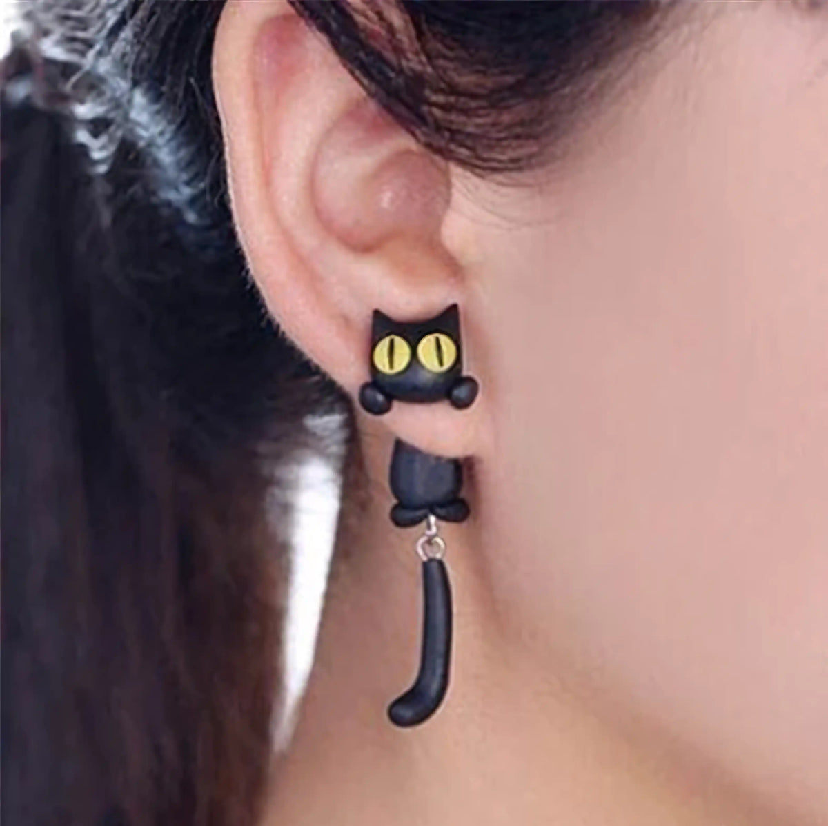 Black cat Tiny Biter earrings worn on an ear